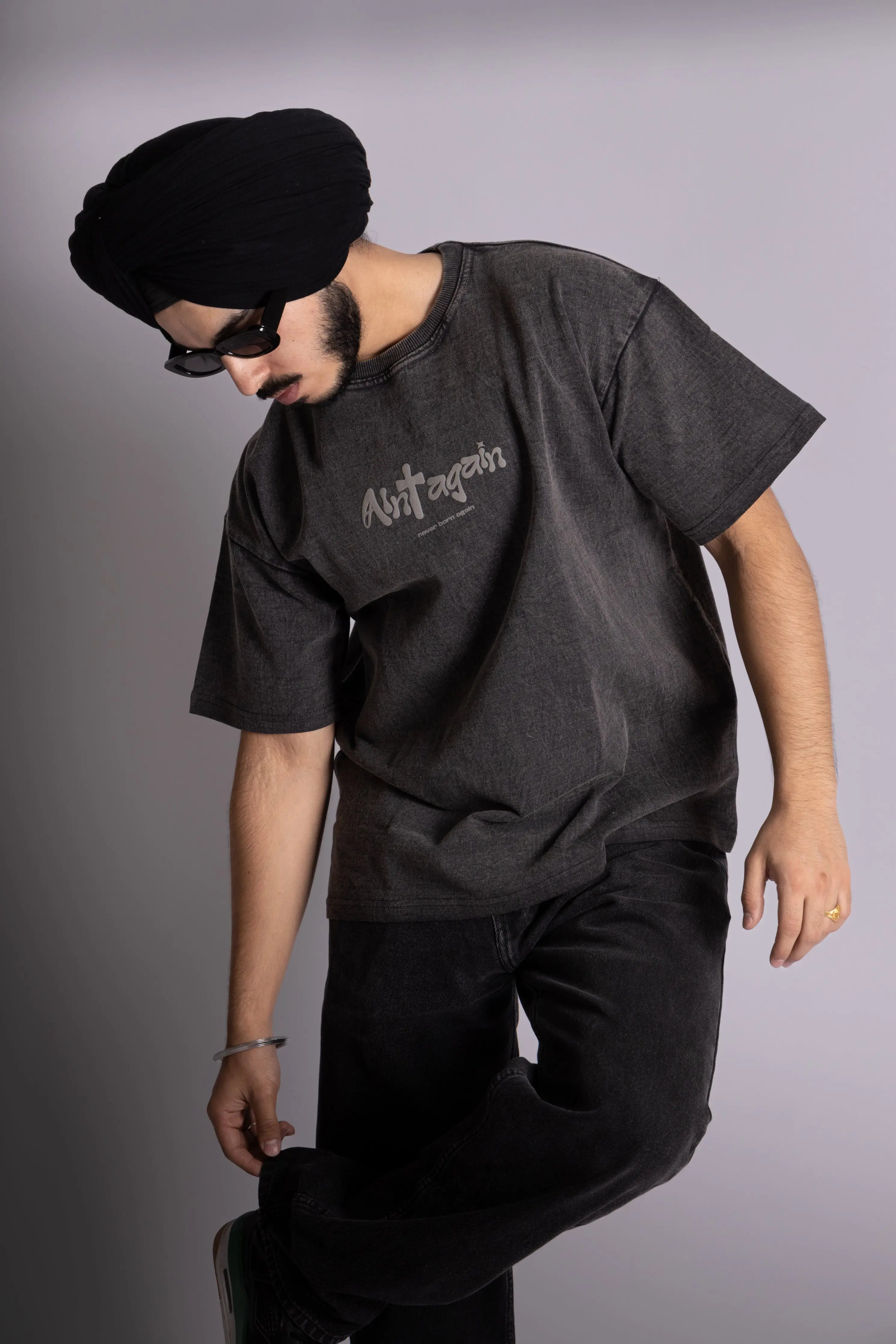 A man wearing stonewash black oversized T-shirt showing the front puff print text.