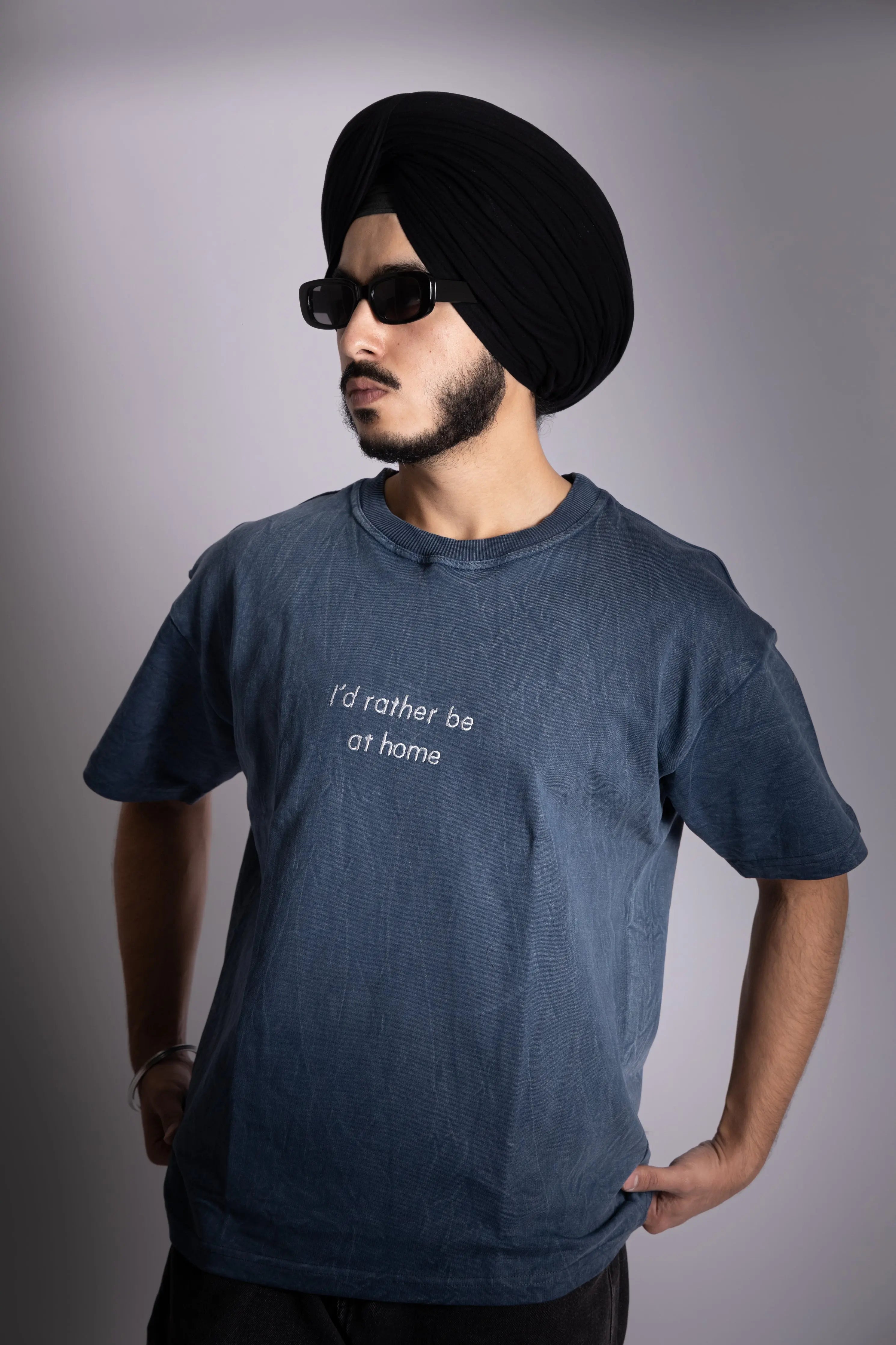 A man wearing stonewash blue oversized T-shirt with embroided text in front.