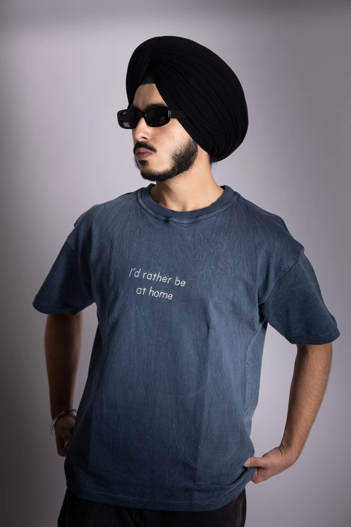 A man wearing stonewash blue oversized T-shirt with embroided text in front.