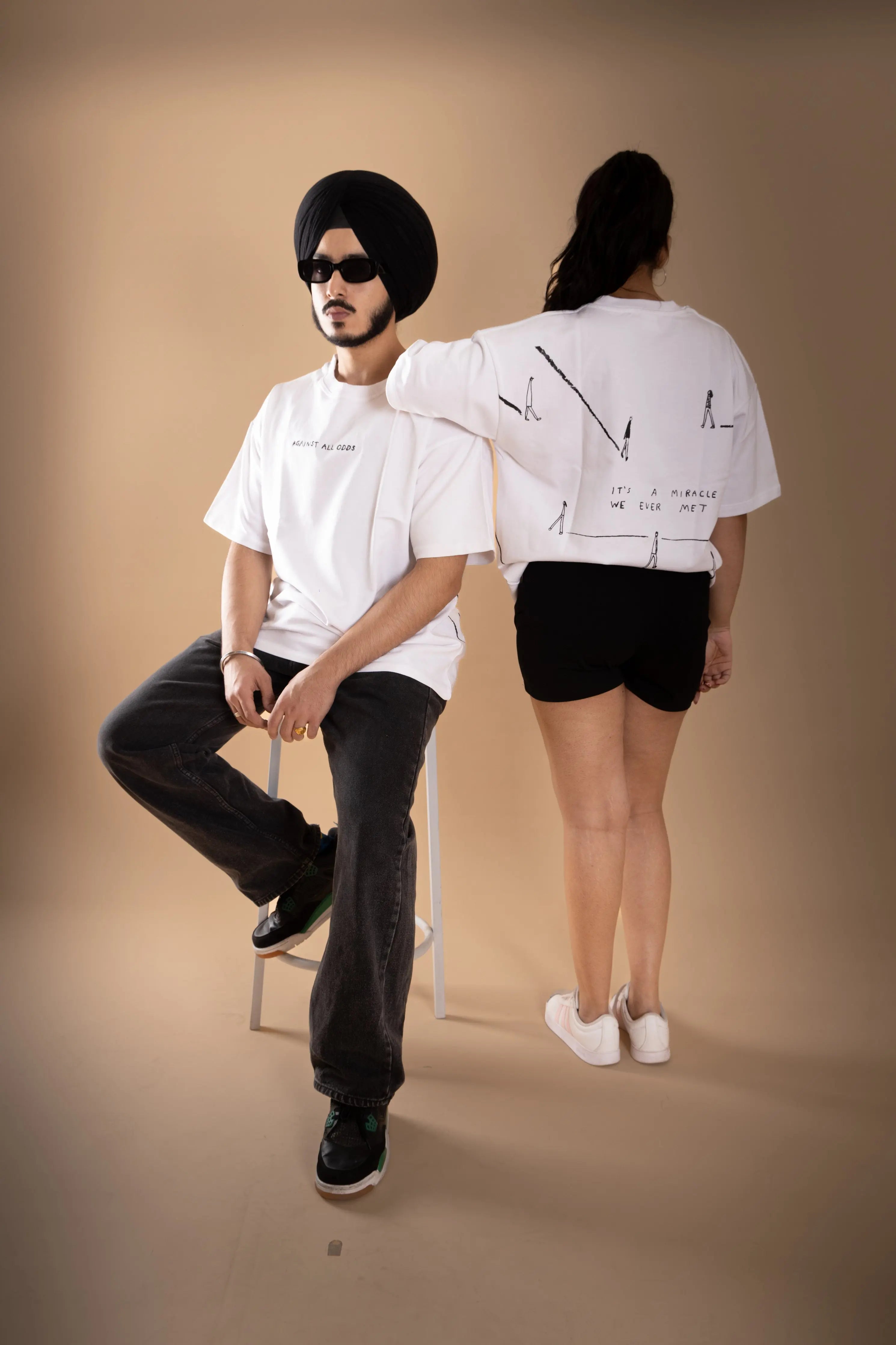 A man and a women standing wearing white oversized T-shirt showing the print.