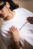 A woman wearing white oversized T-shirt showing the front embroided text.