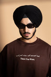 A man wearing brown oversized T-shirt showing the front puff print text.